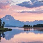 Paisagem serena ao amanhecer com cores suaves, um lago calmo refletindo o céu e montanhas ao fundo, transmitindo paz e inspiração