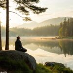 Pessoa meditando em paz próxima a um lago sereno ao amanhecer