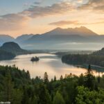 Paisagem tranquila ao amanhecer com luz suave iluminando um lago calmo cercado por vegetação e montanhas ao fundo.