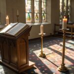 Interior de uma igreja iluminada por vitrais, com uma Bíblia aberta em um púlpito de madeira e velas acesas ao redor, simbolizando a liturgia do dia 14/05/2025