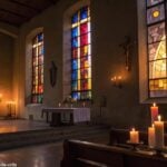 Imagem de uma igreja tranquila com luz suave filtrando através de vitrais, uma bíblia aberta no altar, velas acesas e uma atmosfera serena, evocando reflexão e oração para o dia.