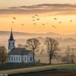 Imagem de um nascer do sol sobre uma igreja no campo, transmitindo paz e bençãos para esta quarta-feira abençoada