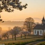 Amanhecer tranquilo sobre uma capela no campo com luz dourada e flores ao redor