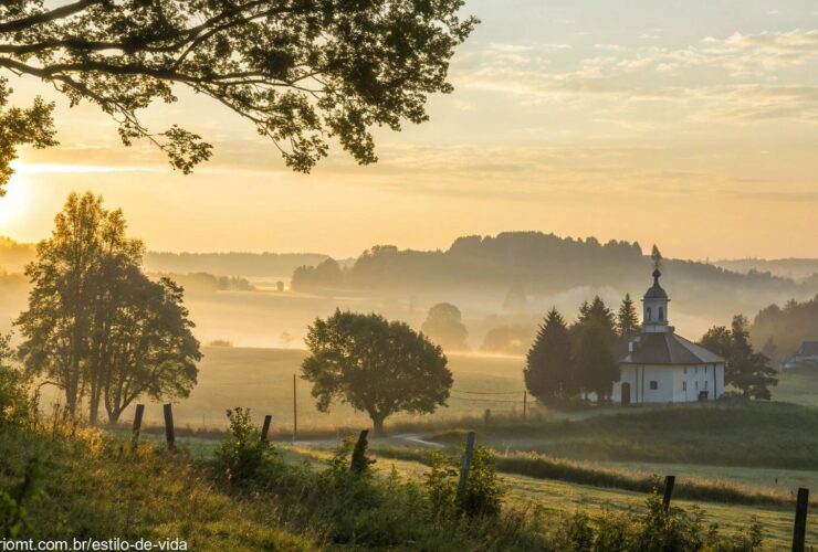 Nascer do sol sereno sobre o campo com uma igreja ao fundo, representando fé e reflexão