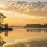 Paisagem serena para a Oração do Dia com um amanhecer tranquilo sobre um lago calmo.