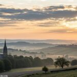 Amanhecer tranquilo sobre um campo sereno com colinas suaves e uma igreja ao fundo, simbolizando fé e esperança.