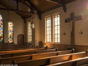Igreja vazia com luz do sol entrando pelos vitrais, iluminando uma cruz de madeira simples no altar, atmosfera tranquila e reflexiva