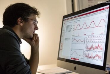 Pessoa pensativa analisando gráficos matemáticos com tons de vermelho e branco, representando a Dupla Sena.