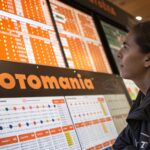 Pessoa curiosa examinando gráficos de probabilidade e valores de prêmios em um display digital com tons de laranja e branco.