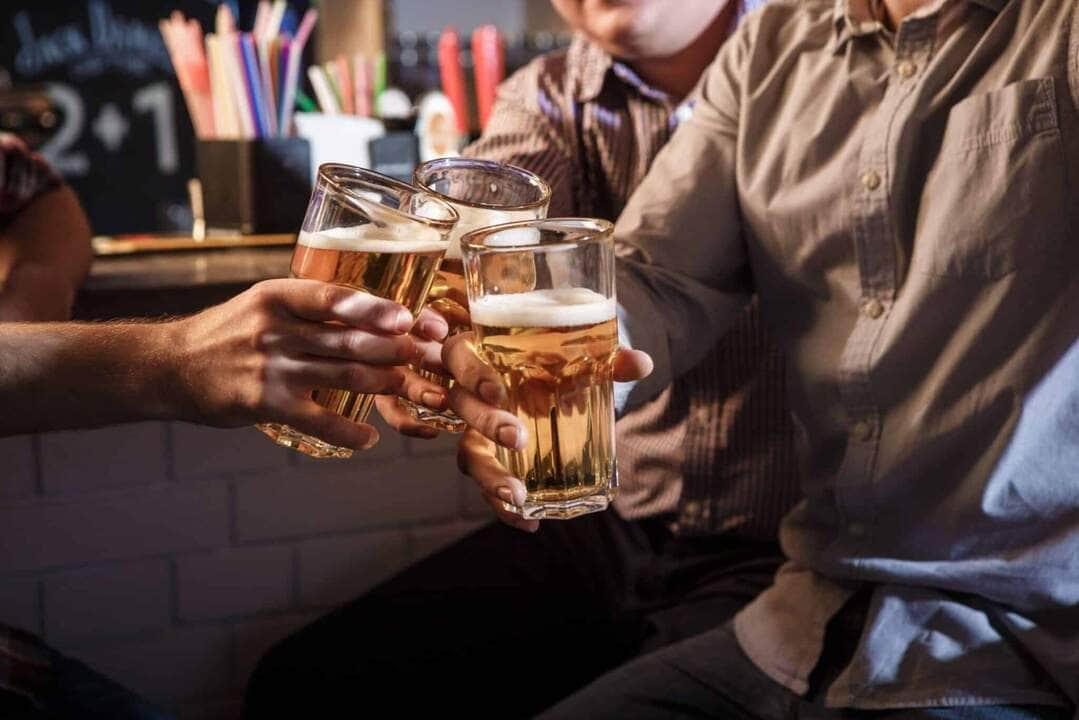 happy friends drinking beer at counter in pub scaled