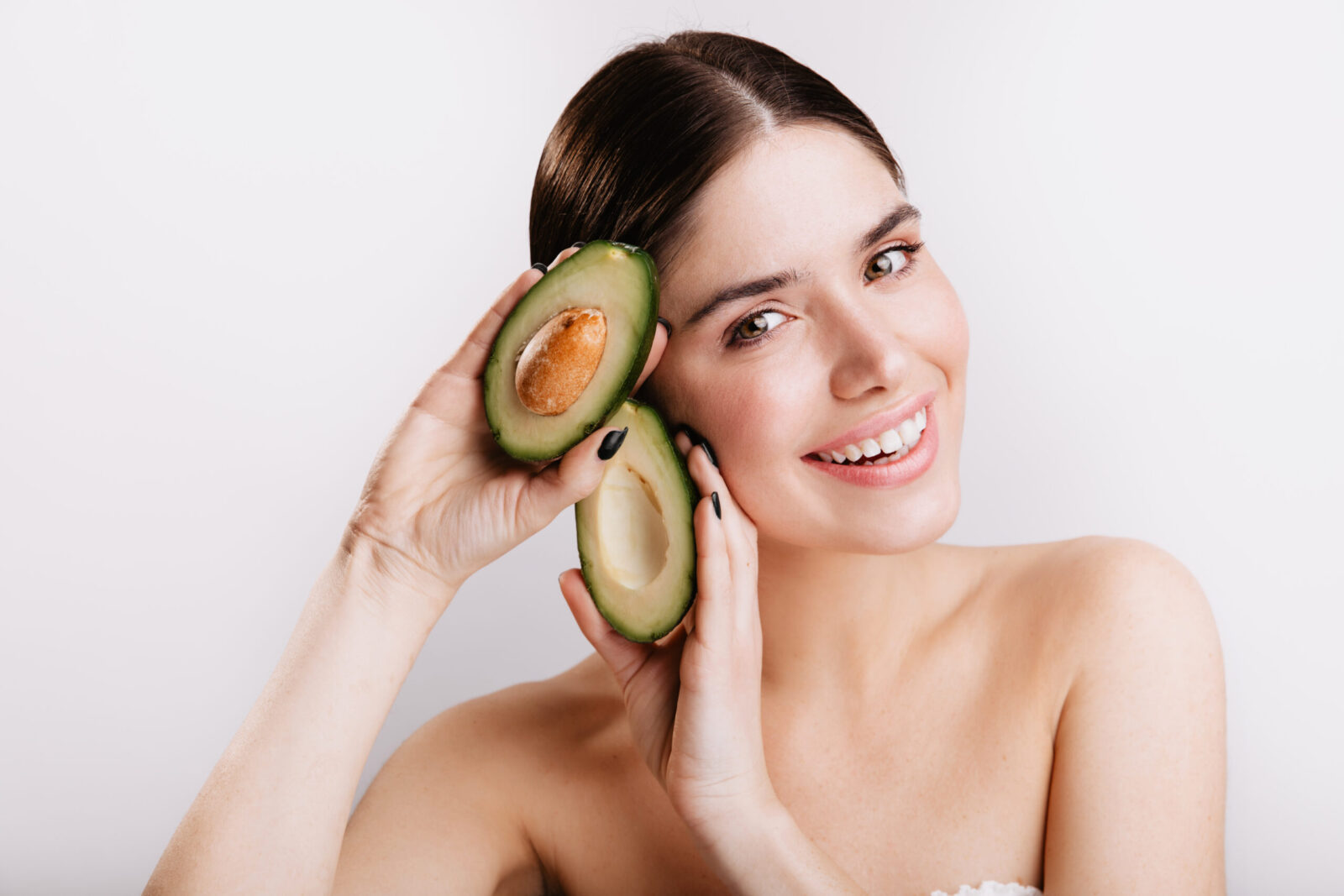 close up de uma mulher sorridente de olhos verdes sem maquiagem na parede branca o modelo demonstra beneficios para a pele do abacate scaled 1