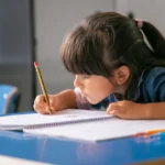 garota latina de cabelo concentrado sentada na mesa da escola e desenhando em seu caderno 74855 16368