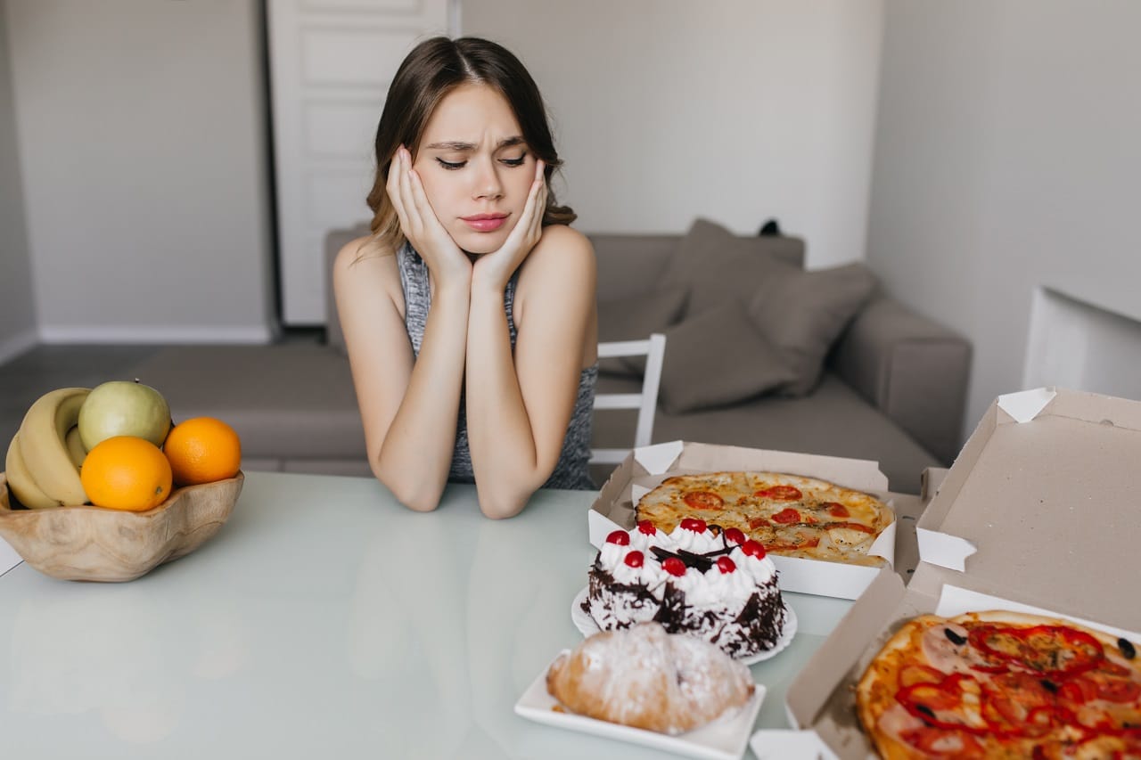 mulher encaracolada triste olhando para o bolo durante a dieta loira linda modelo feminino posando com frutas e pizza