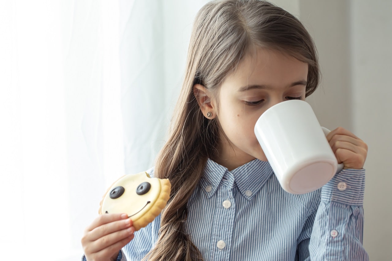 uma menina da escola primaria esta tomando cafe da manha com leite e biscoitos engracados na forma de um smiley