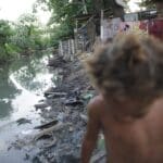 Imagem de riacho com falta de saneamento básico e uma criança passando em favela do Complexo da Maré Por: Arquivo/Fernando Frazão/Agência Brasil