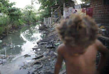 Imagem de riacho com falta de saneamento básico e uma criança passando em favela do Complexo da Maré Por: Arquivo/Fernando Frazão/Agência Brasil