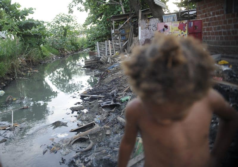 Imagem de riacho com falta de saneamento básico e uma criança passando em favela do Complexo da Maré Por: Arquivo/Fernando Frazão/Agência Brasil