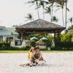 casal jovem elegante e hippie apaixonado andando e brincando com um cachorro em uma praia tropical