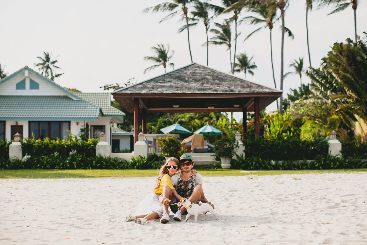 casal jovem elegante e hippie apaixonado andando e brincando com um cachorro em uma praia tropical
