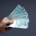 Dinheiro brasileiro na mão em um fundo cinza - Fotos do Canva