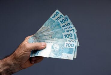 Dinheiro brasileiro na mão em um fundo cinza - Fotos do Canva