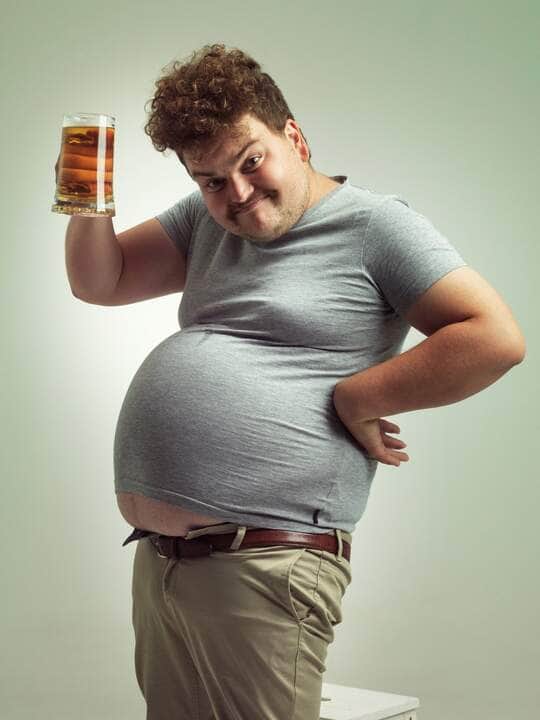 Pessoa com barriga grande segurando copo de cerveja - Fotos do Canva