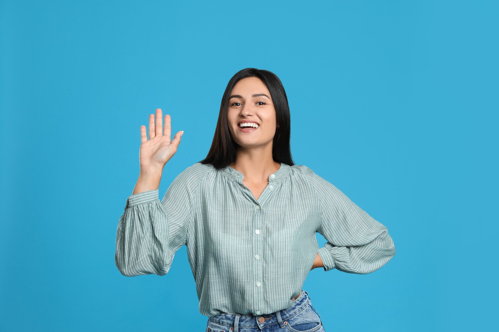 Mulher feliz acenando para dizer olá sobre fundo azul claro - Fotos do Canva