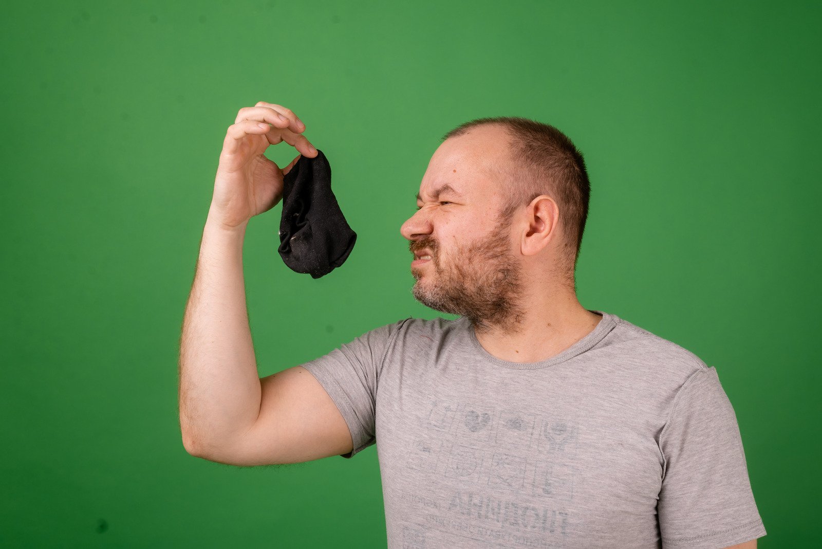 Middle Aged Man Sniffing Smelly Sock on Green Background. Laundry, Hygiene, Smelly Feet Concept. - Fotos do Canva