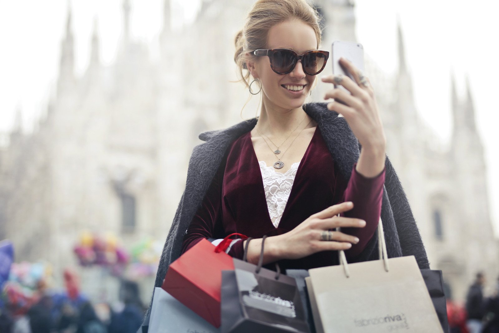 Mulher de blusa marrom de mangas compridas segurando smartphone com sacolas de compras durante o dia - Fotos do Canva