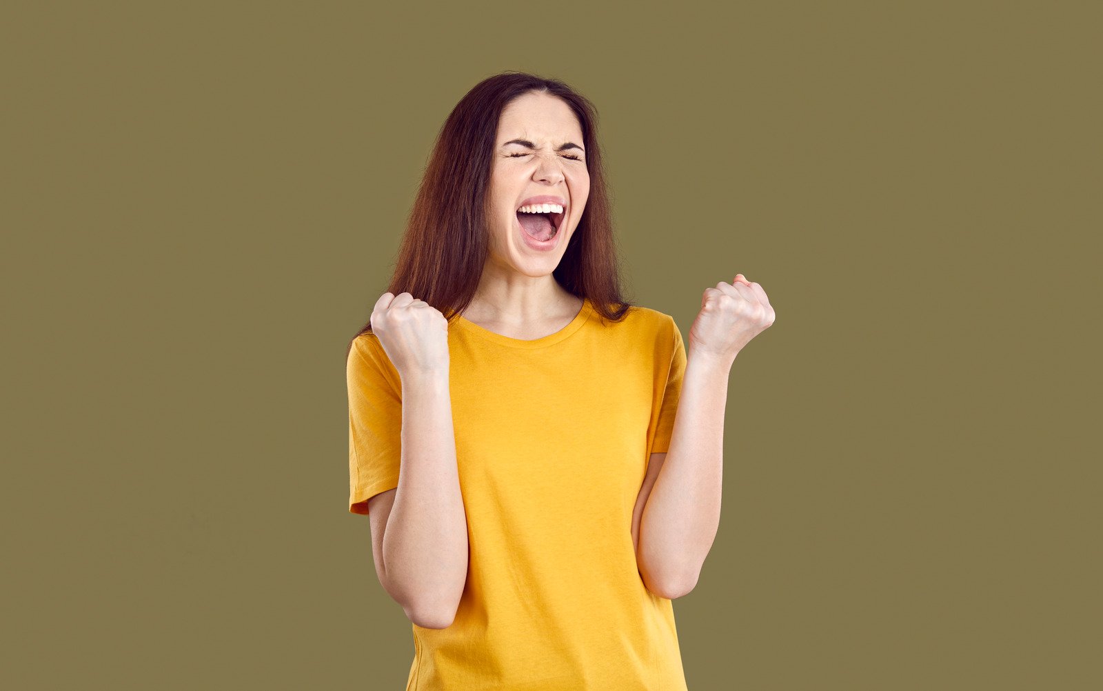 Mulher louca e feliz feliz isolada em fundo marrom, apertando os punhos e gritando sim - Fotos do Canva