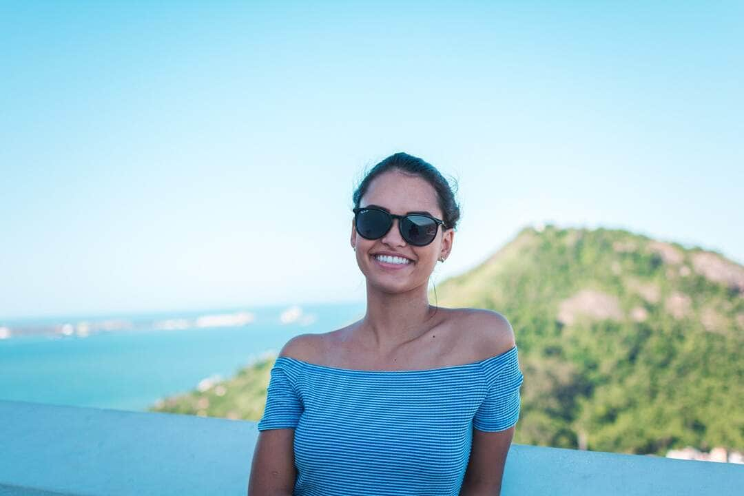 Mulher sorridente usando blusa ombro a ombro listrada cinza e óculos de sol pretos - Fotos do Canva