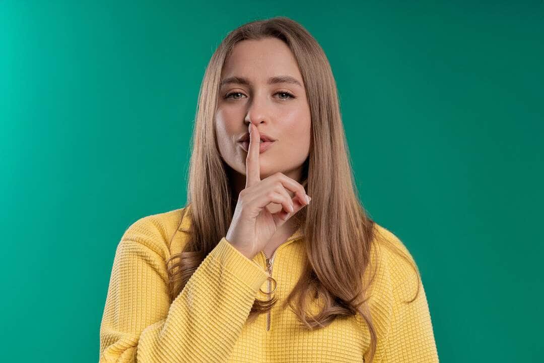 Smiling pretty woman with finger on lips - shhh, secret, silence, blue studio - Fotos do Canva
