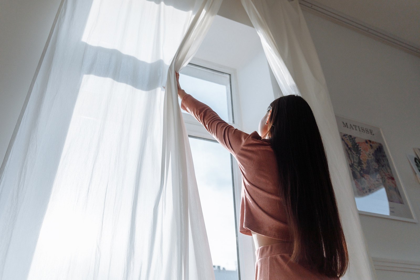 Uma mulher abrindo uma cortina branca - Fotos do Canva