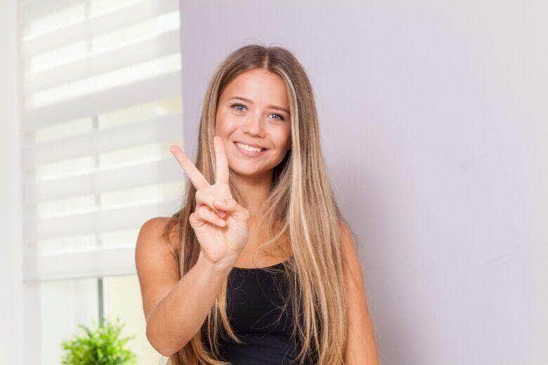 Menina loira sorrindo fazendo sinal de vitória com a mão, selecionada - Fotos do Canva
