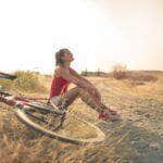 Mulher esportiva com bicicleta descansando em uma estrada rural sob a luz do sol - Fotos do Canva