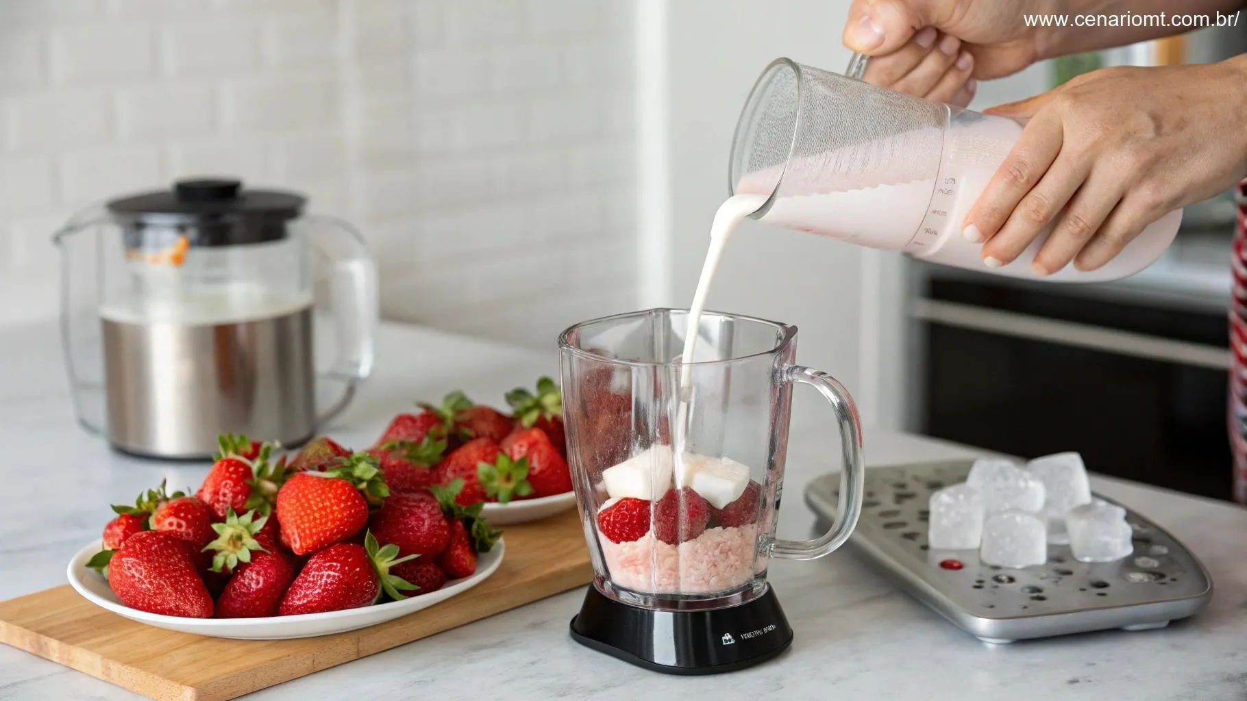 Preparação do smoothie de morango: mão vertendo iogurte no liquidificador com morangos e gelo ao lado