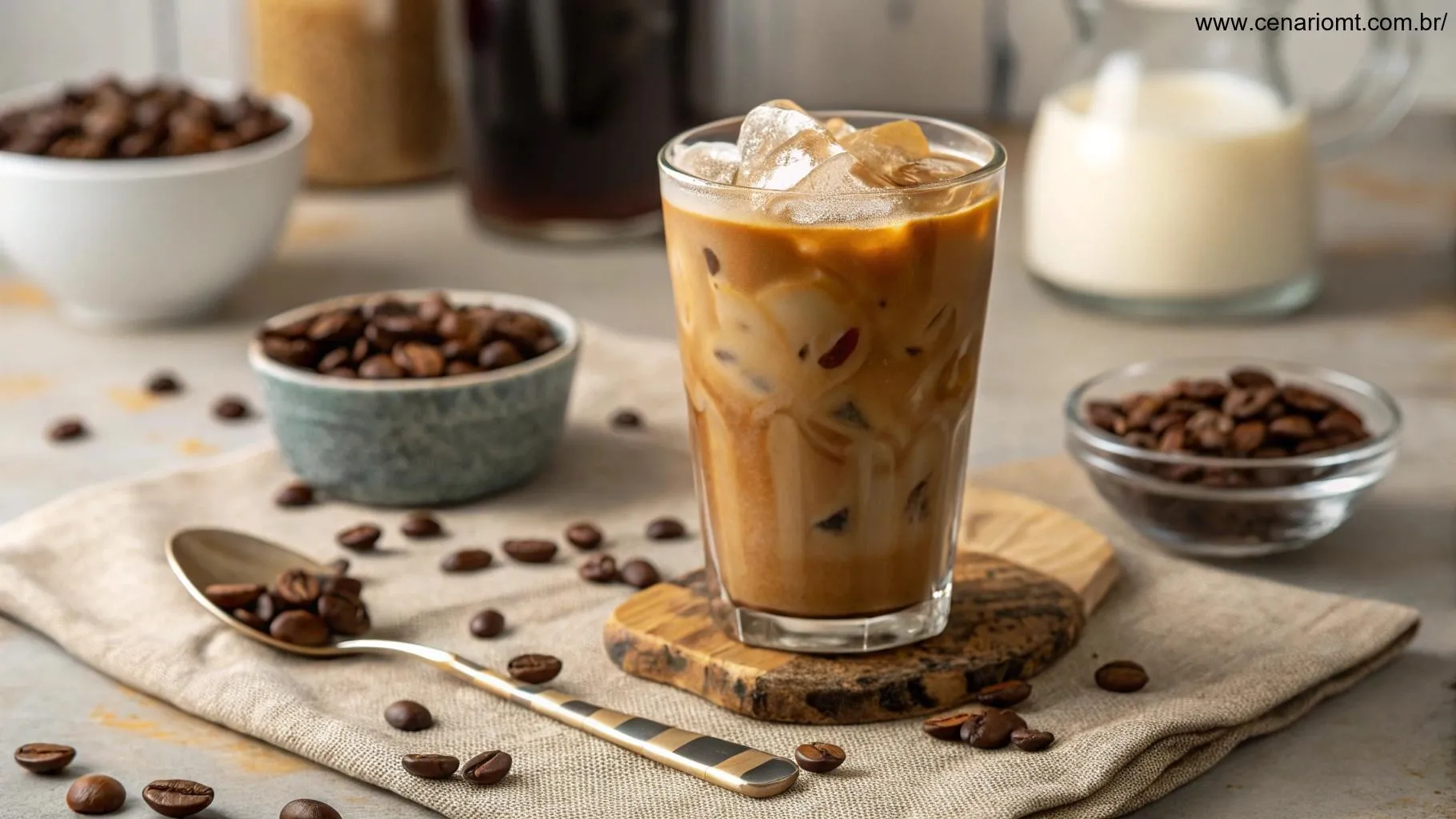 Café gelado com uma camada espessa de creme, rodeado por grãos de café e uma colher, com fundo desfocado de uma cozinha aconchegante.