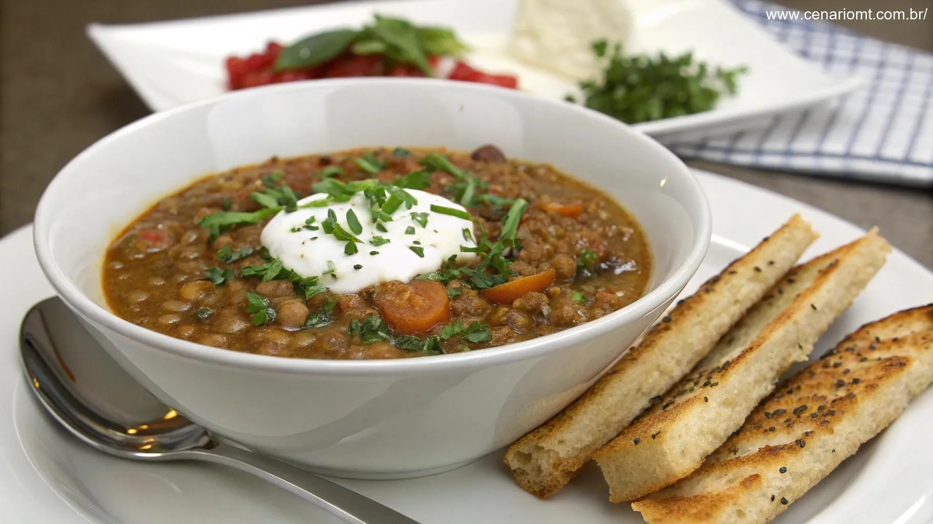 Uma tigela de sopa de lentilha lindamente decorada com creme azedo, cebolinha picada e acompanhada de palitos de pão torrados, criando uma apresentação gourmet.