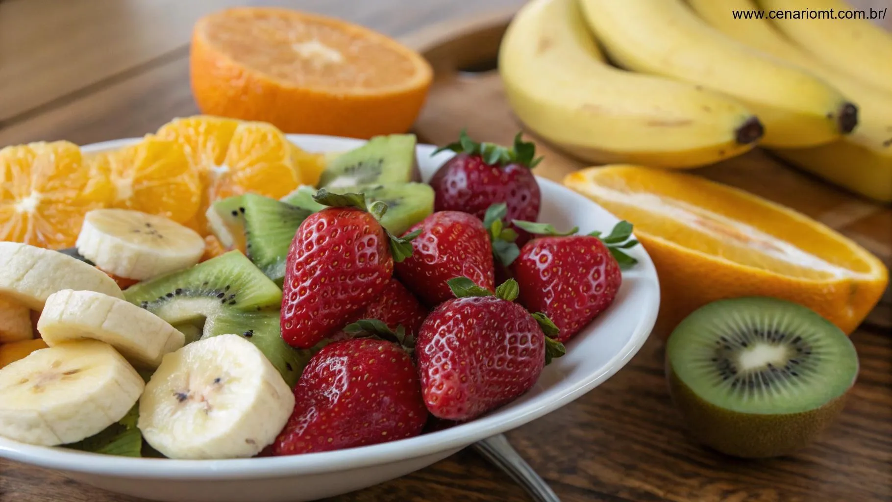 Ingredientes frescos para uma salada de frutas, incluindo bananas maduras, morangos suculentos, laranjas brilhantes e kiwis fatiados, dispostos sobre uma mesa de madeira.