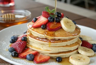 Uma pilha de panquecas americanas fofinhas com frutas frescas e mel.