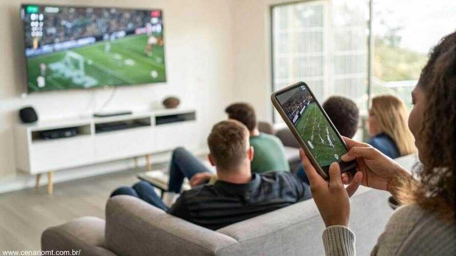 Pessoas assistindo um jogo de futebol entre Rayo Vallecano e Real Valladolid em uma televisão e celular, com foco em estatísticas ao vivo.