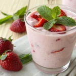 Smoothie cremoso de morango com iogurte servido em um copo transparente com morango e folha de hortelã