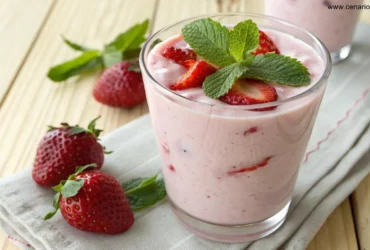 Smoothie cremoso de morango com iogurte servido em um copo transparente com morango e folha de hortelã