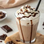 Milkshake de chocolate cremoso servido em um copo alto com chantilly e calda de chocolate por cima.