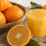 Um copo de suco de laranja recém-espremido com algumas laranjas ao redor, mostrando uma cor laranja vibrante, natural e saudável.