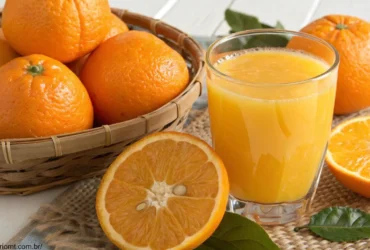 Um copo de suco de laranja recém-espremido com algumas laranjas ao redor, mostrando uma cor laranja vibrante, natural e saudável.